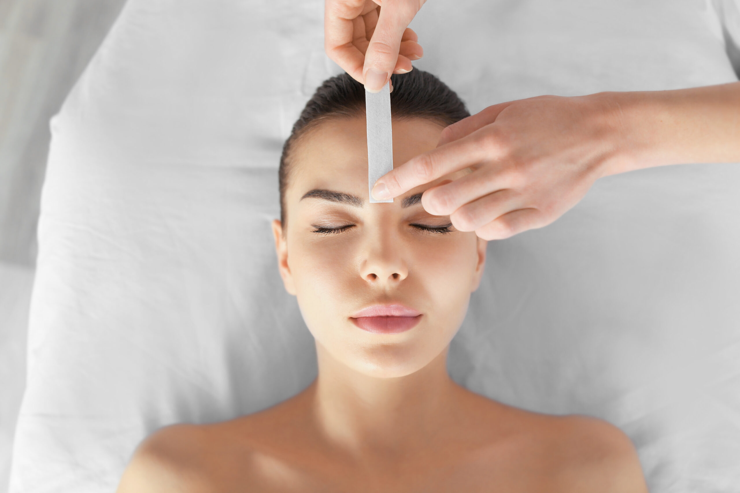 esthetician waxing a young woman's eyebrows in a salon