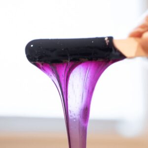 Purple soft wax being applied with a wooden applicator stick